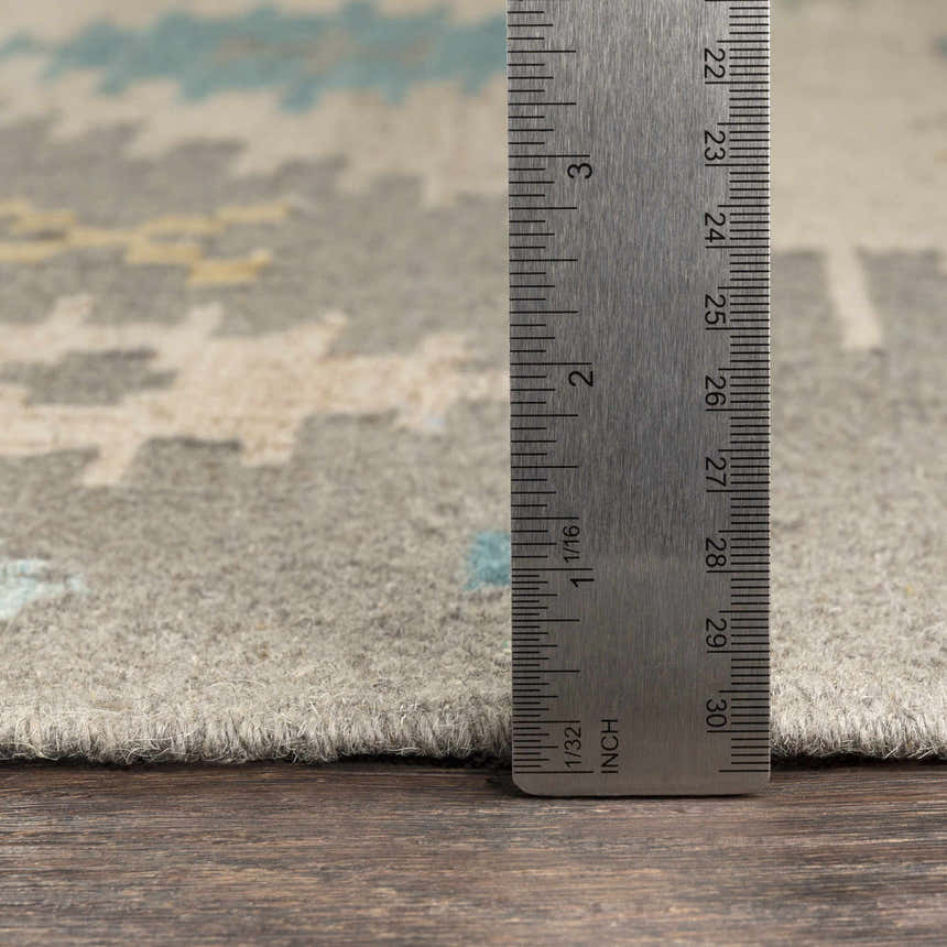 Close-up of the Heth Carpet showing the pile height with a ruler. Beige, blue, and charcoal wool rug texture. Pile