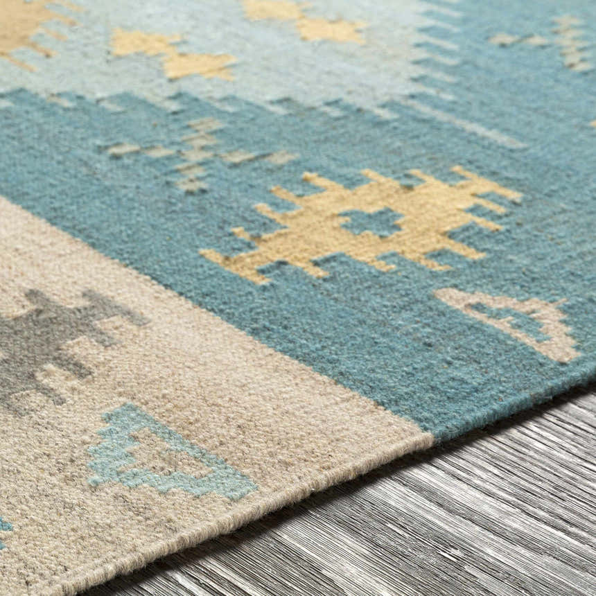 Close-up of the hand woven Heth Carpet. Features beige, blue, and tan geometric patterns on a wool texture. Texture
