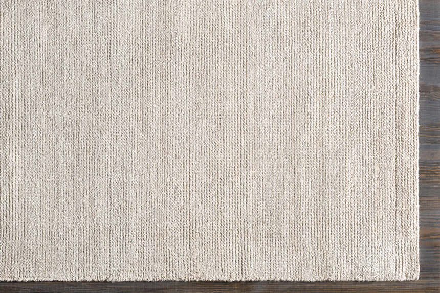 Close up of the ivory Hookstown Area Rug showing hand woven texture on dark wood floor. Corner