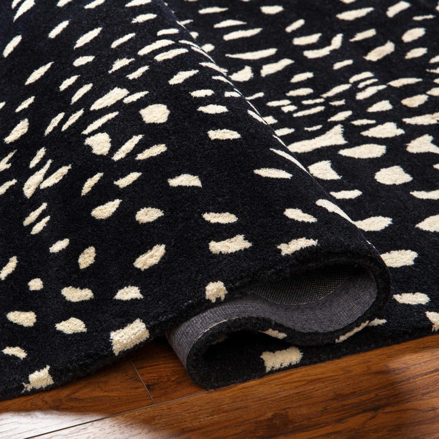 Close-up of rolled Athena Black Giraffe Print Wool Rug showing black background and beige animal print. Fold
