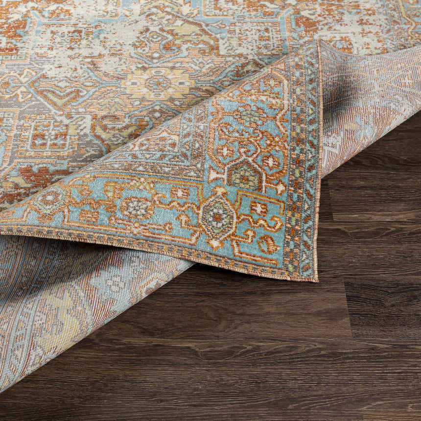Close up of the Hardwick Performance Rug showing its bohemian pattern and colors of brick red, brown, charcoal, and pale blue. Fold