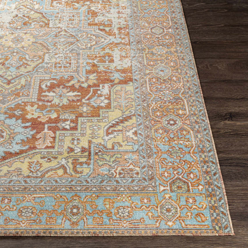 Close-up of the Hardwick Performance Rug showing its brick red, blue, and saffron traditional pattern on dark wood floor. Front