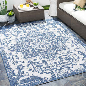 Outdoor patio scene with a Dark Blue Kilmacolm Indoor & Outdoor Area Rug, wicker furniture, and potted plants. Roomscene-Rectangle