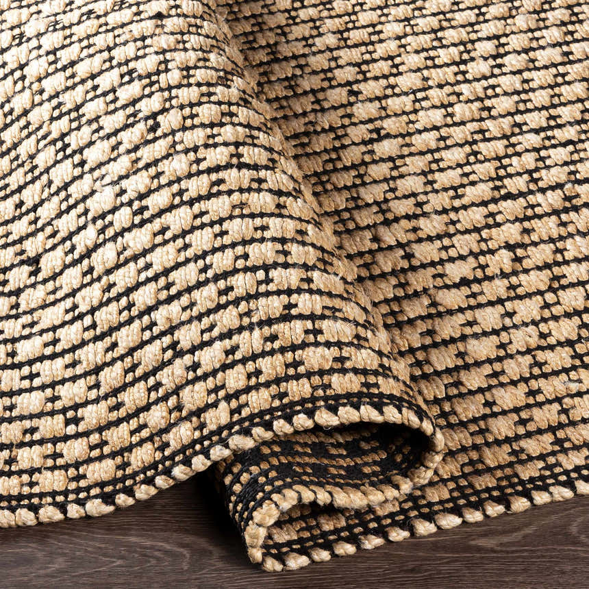 Close-up of the hand-woven Iqaluit Natural Jute Rug. Features a black and light beige geometric pattern and textured design. Fold