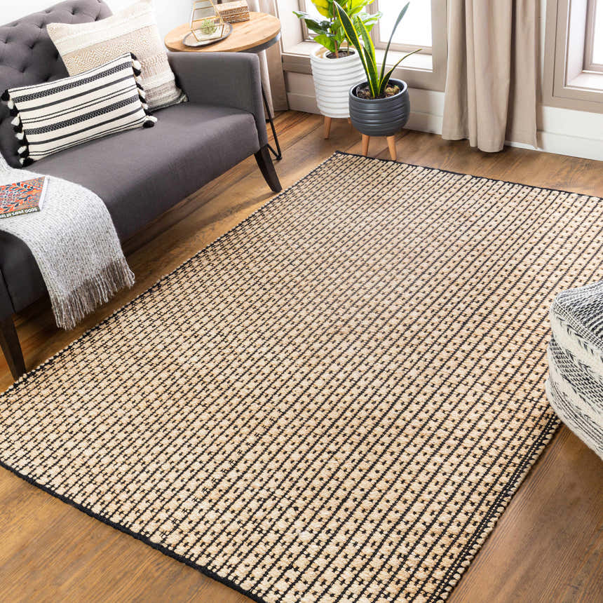 Living room scene with a black and beige Iqaluit Natural Jute Rug, gray sofa, plants, and wood floors. Roomscene-Rectangle