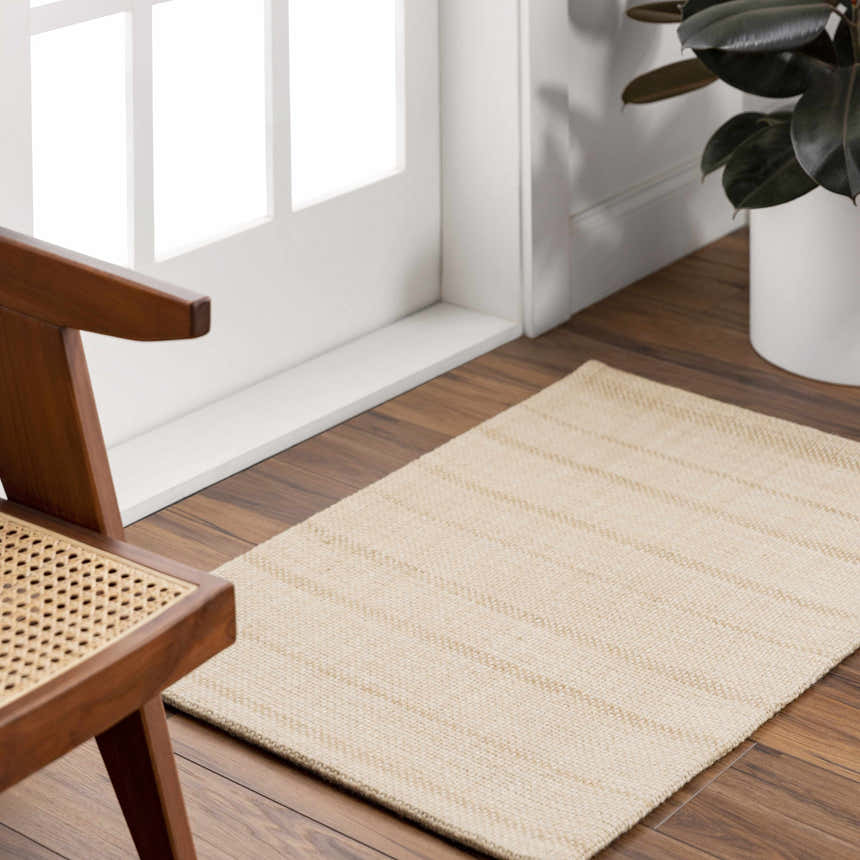 Entryway scene with a tan Javon Area Rug, wood floors, white door, and a mid-century modern chair. Roomscene-Rectangle