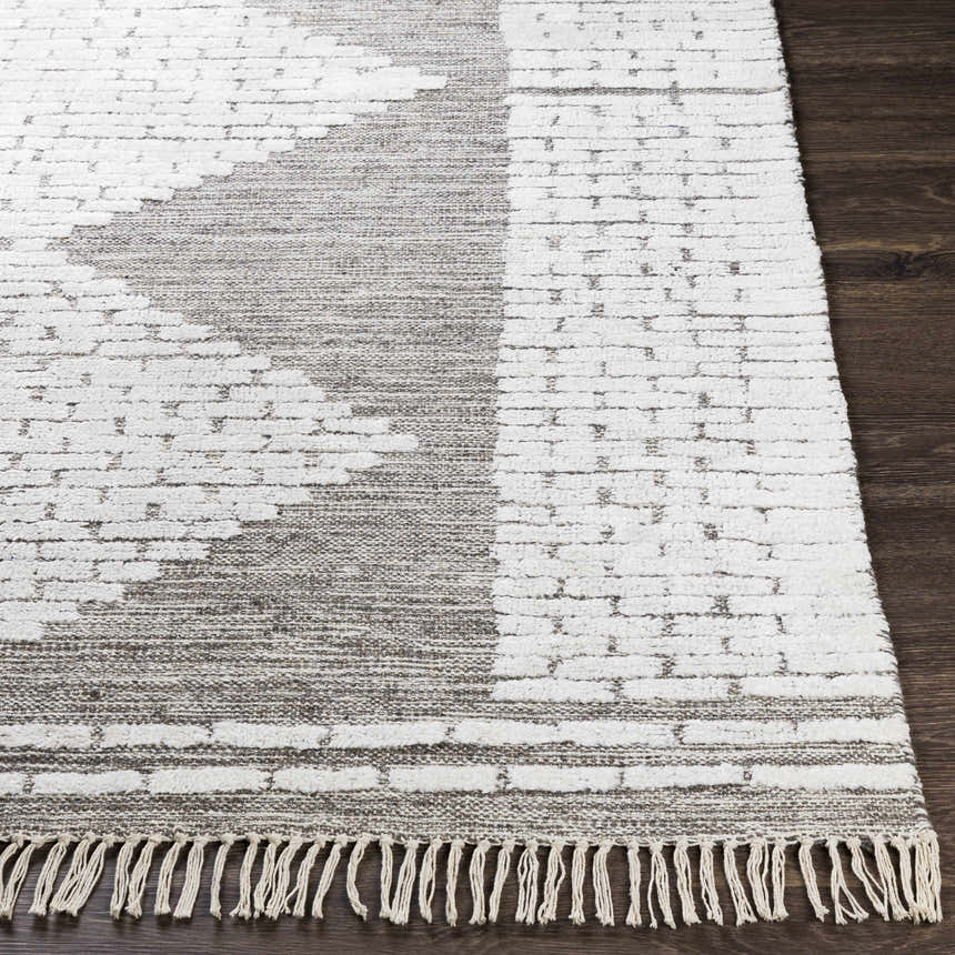 Close-up of the Junction Carpet - Clearance. Hand-woven wool rug in brown, beige, and white with a geometric pattern and fringe. Front