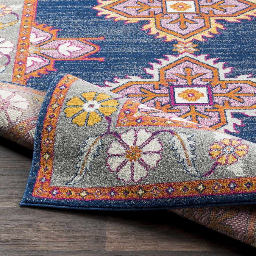 Close-up of the Kaitlyn Navy Area Rug showing its bohemian pattern, floral border, and colors like navy, orange, and gray. Fold