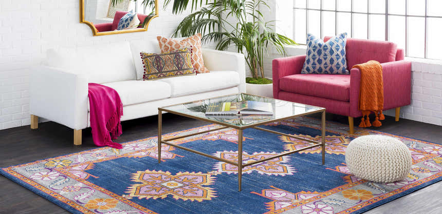 Living room scene with a Kaitlyn Navy Area Rug, white sofa, pink chair, and glass coffee table. Roomscene-Rectangle