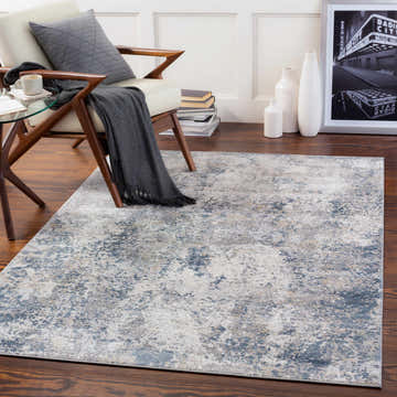 Living room scene with a Kanahooka Area Rug in charcoal, blue, beige, and gray under a chair and glass table. Roomscene-Rectangle