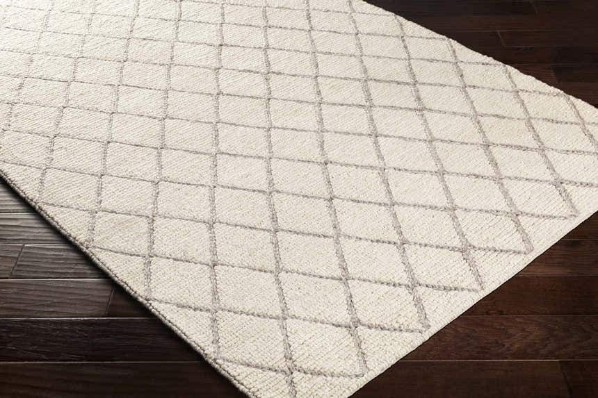 Close-up of the hand woven Kanopolis Carpet. Cream rug with a medium gray geometric diamond pattern. Corner