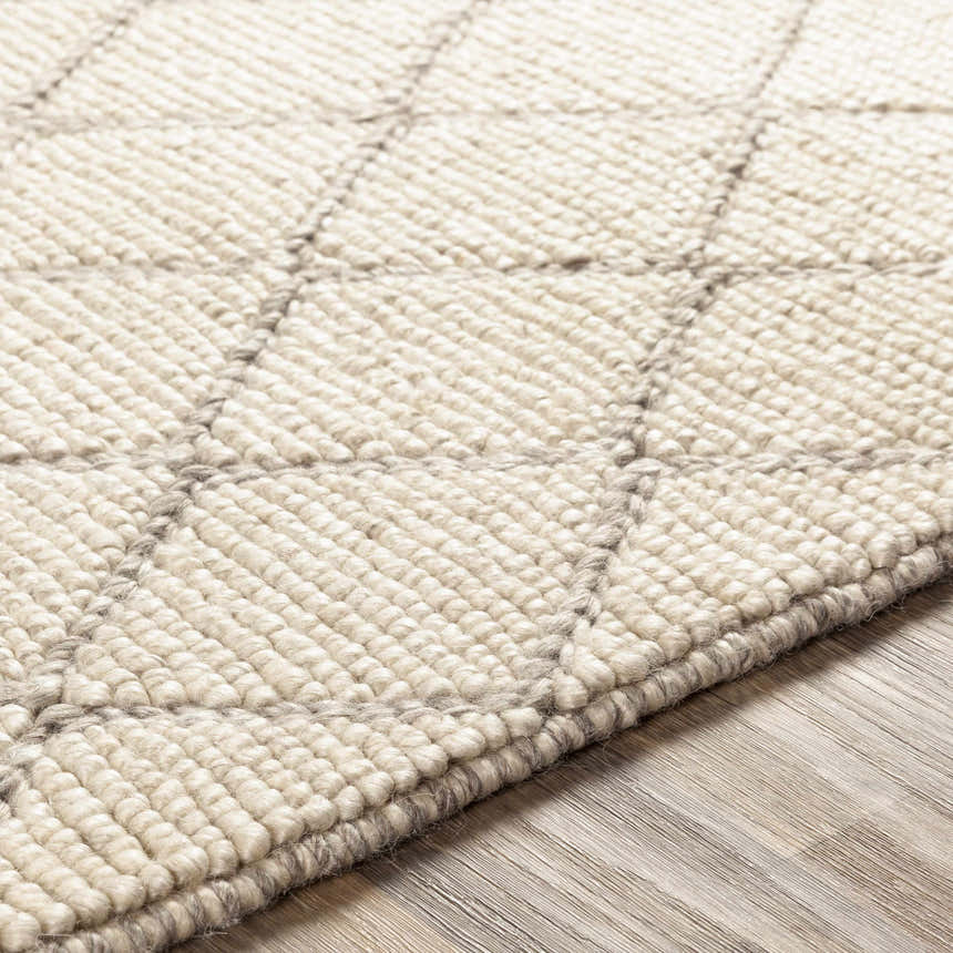 Close-up of the hand woven Kanopolis Carpet. Cream wool rug with a gray diamond pattern and textured pile. Texture