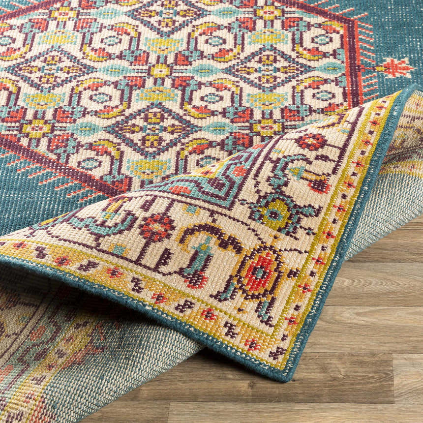Close-up of the hand-knotted Kaser Carpet. Farmhouse style rug features dark plum, beige, green, and teal colors. Fold