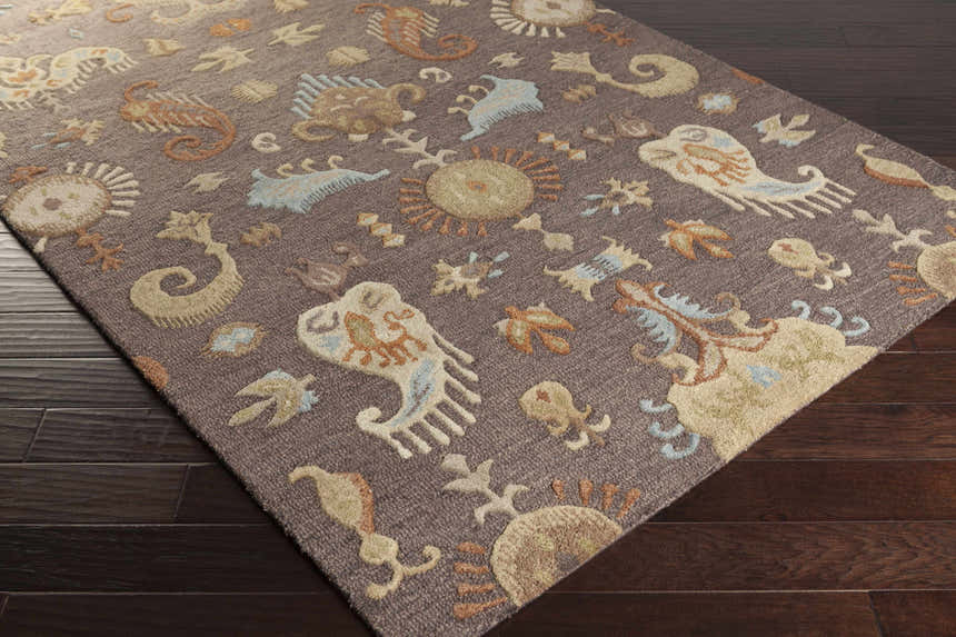 Close-up of the Kelty Area Rug showing a hand-hooked design with beige, orange, and blue accents on a gray wool rug. Corner