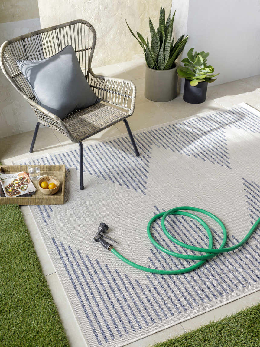 Outdoor patio scene with a cream and navy geometric Khandallah Area Rug, wicker chair, and garden hose. Roomscene-Rectangle