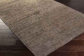 Close-up of the hand-woven Kingwood Area Rug. Dark and light brown viscose rug with subtle texture on dark wood flooring. Corner