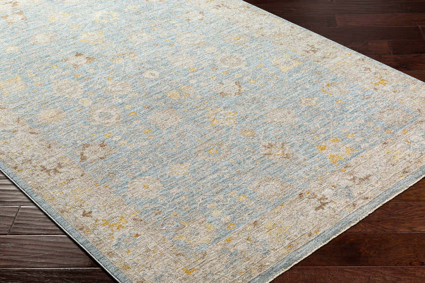 Close-up of Kofi Thick Luxe Area Rug. Traditional style rug in amber, taupe, light olive and blue on dark wood floor. Corner