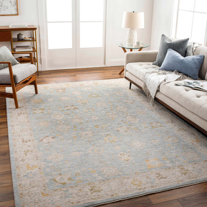 Living room scene featuring the Kofi Thick Luxe Area Rug in amber, brown, and olive tones. Beige sofa, wood floors, and natural light. Roomscene-Rectangle