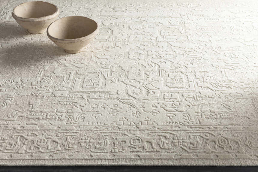 Close-up of the ivory Larimer Area Rug with a raised, textured pattern and two decorative bowls. Styleshot