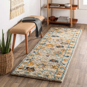 Hallway scene with a Lordstown Luxury Wool Oushak Rug, beige bench, wood shelf, and woven wall art. The rug has beige, blue, and mustard tones. Roomscene-Runner
