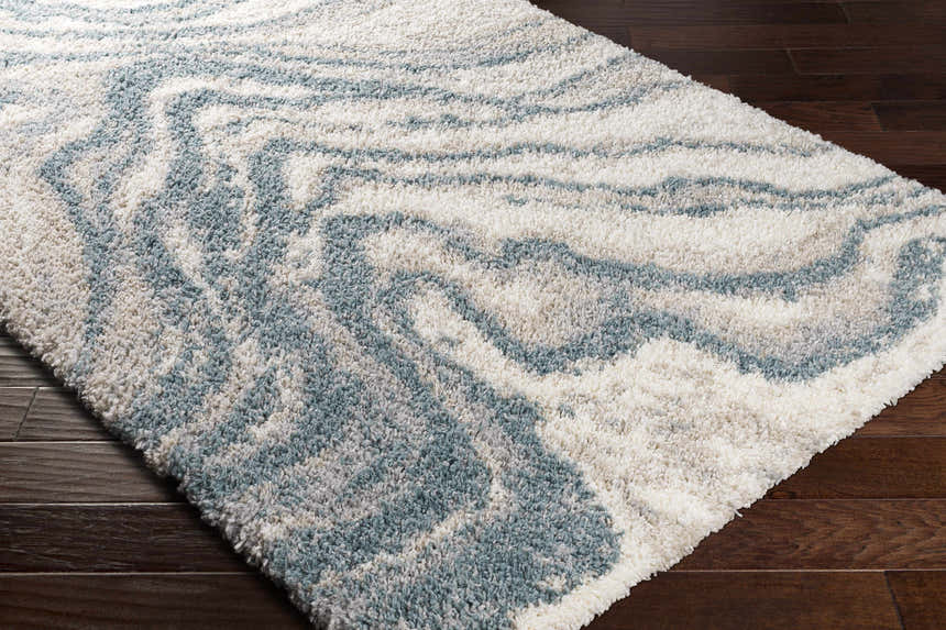 Close-up of the Lottery Area Rug; a blue and cream shag rug with a contemporary, abstract pattern. Corner