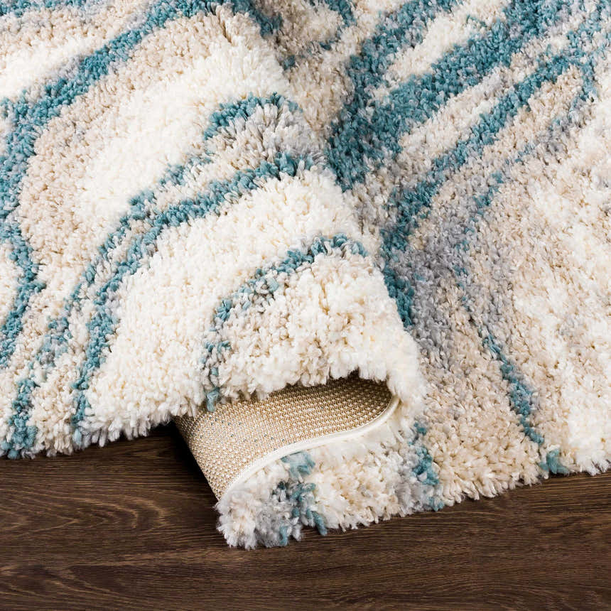 Close-up of the Lottery Area Rug, a shag rug with blue, cream, beige, and gray wavy stripes. Fold