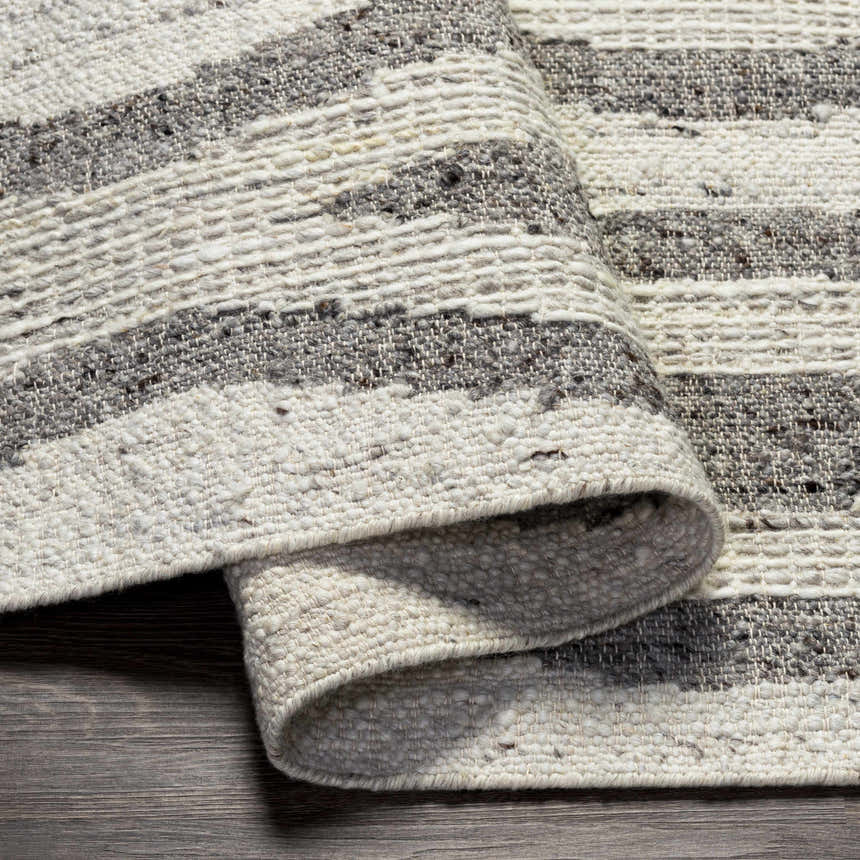 Close-up of Lavalwaves rug showing hand woven wool texture and brown, charcoal, cream, and gray stripes. Fold