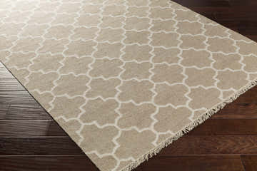 Close-up of the hand-woven Lydia Area Rug. Cream and tan wool rug with a quatrefoil pattern and fringed edge. Corner
