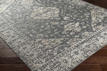 Close-up of the Macgregor Area Rug showing its charcoal base and light gray, hand-loomed, bohemian-inspired pattern and texture. Corner