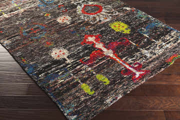 Close-up of the Macy 5x8 Handmade Black Silk Carpet. Features brick red, dark green, and denim accents on a dark background. Corner
