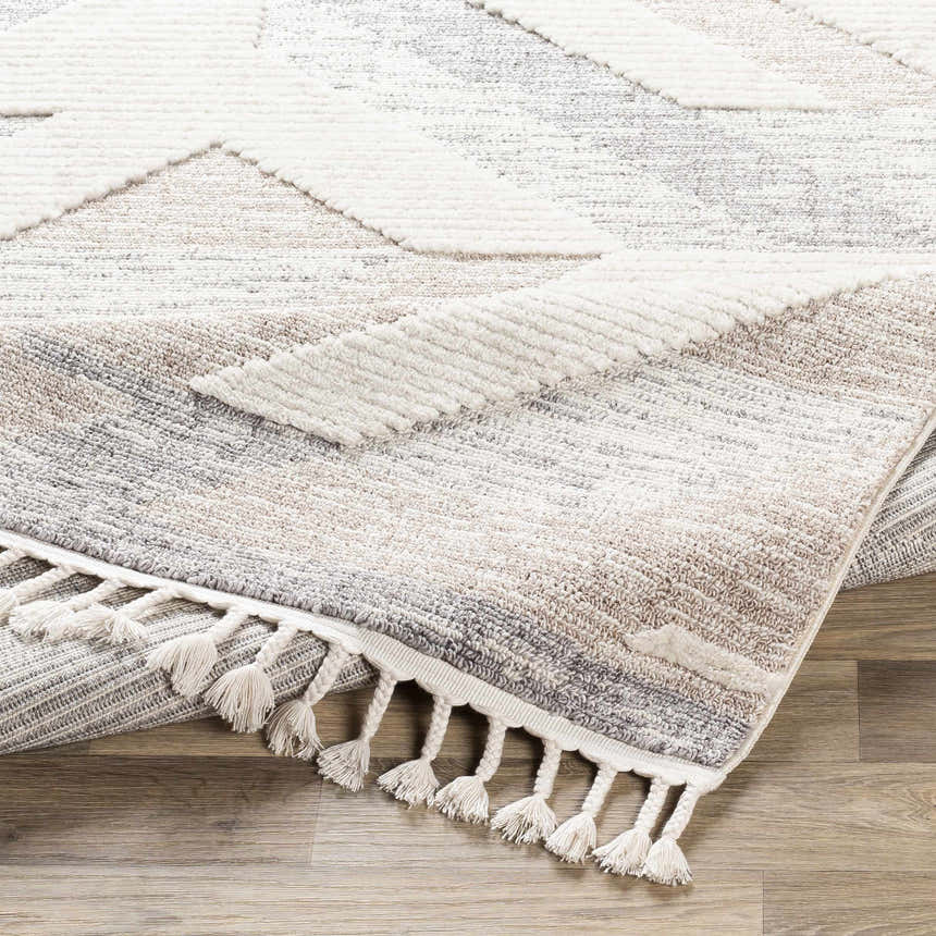 Close up of Magazine Geometric High/Low Pile Rug with tassels. Gray, tan, and white geometric pattern. Tassels detail. Fold