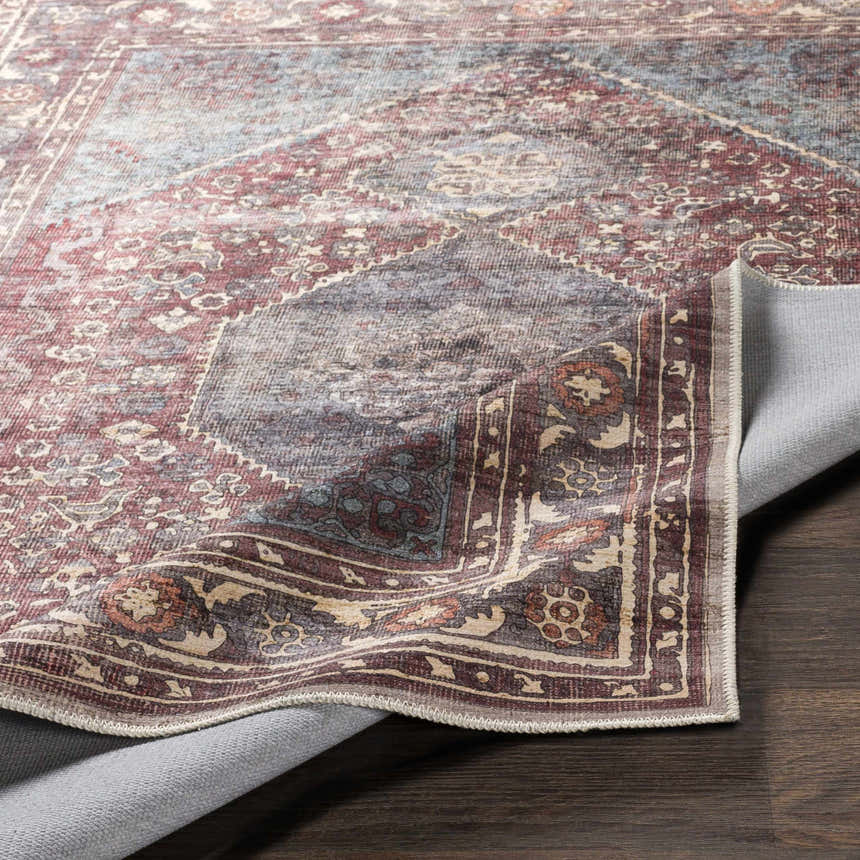 Close-up of the Maplesville Washable Area Rug showing its beige, dark pink, and teal traditional pattern. Fold