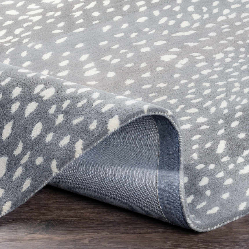 Close-up of the Athena Gray Giraffe Print Wool Rug. Gray rug with cream animal spots and a hand-tufted texture. Fold