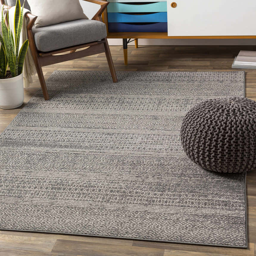 Living room scene with a charcoal Mckinney Area Rug, gray chair, and pouf. The rug features a contemporary geometric pattern. Roomscene-Rectangle