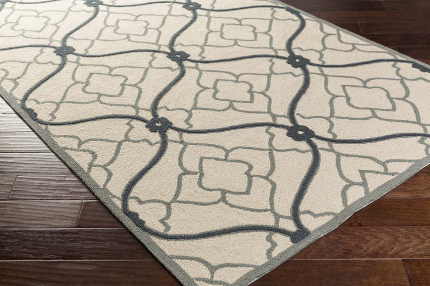 Close-up of the Menomonie Area Carpet. Hand-hooked, light beige rug with a dusty sage and navy geometric pattern. Corner