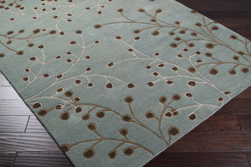 Close-up of the Sage Elsu Area Rug. Sage rug with dark brown floral pattern on dark wood floor. Hand-tufted wool rug. Corner