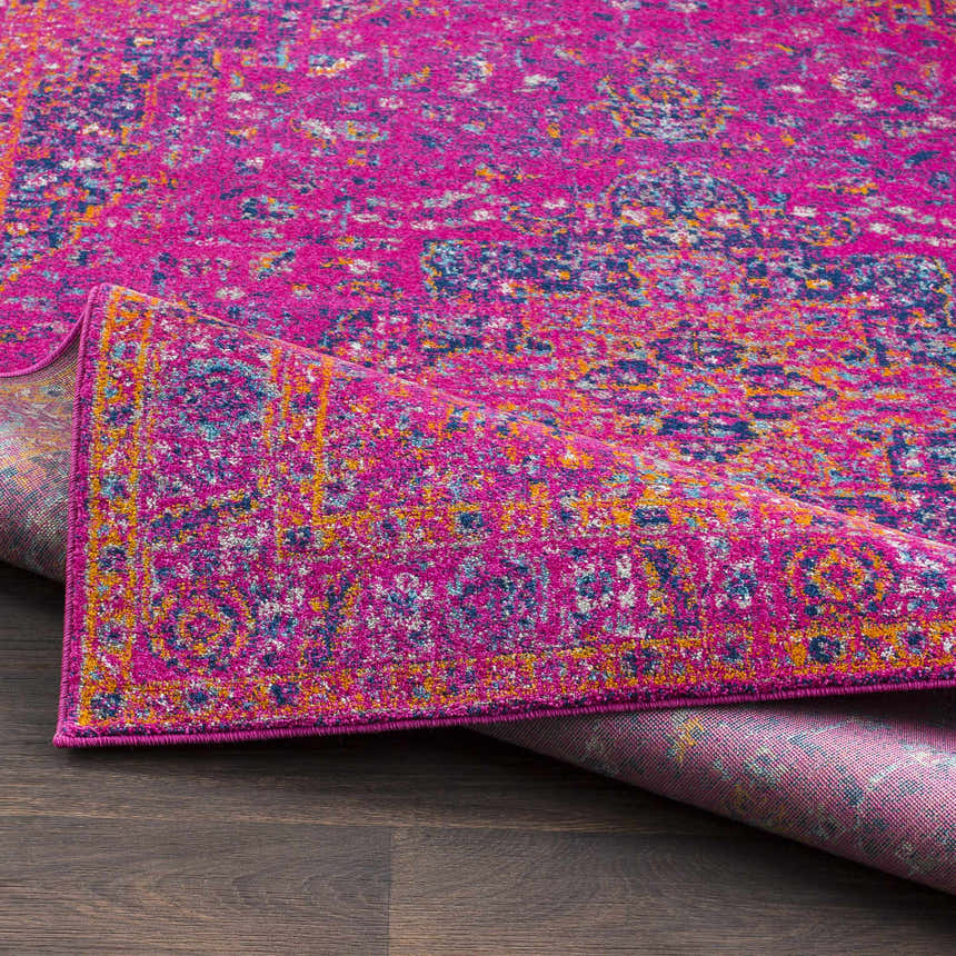 Close-up of the Milliken Magenta Area Rug showing its magenta, teal, navy, and orange traditional pattern. Fold
