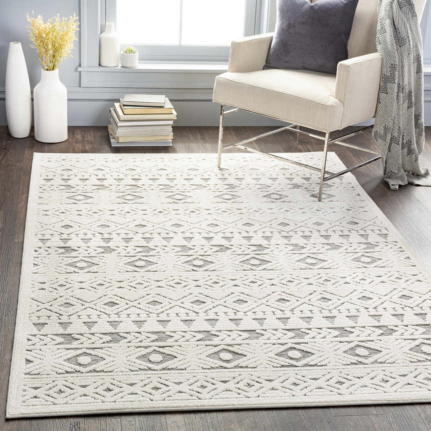 Living room scene with a light beige chair and the Mirani 3D Outdoor Area Rug in charcoal and light beige. Roomscene-Rectangle