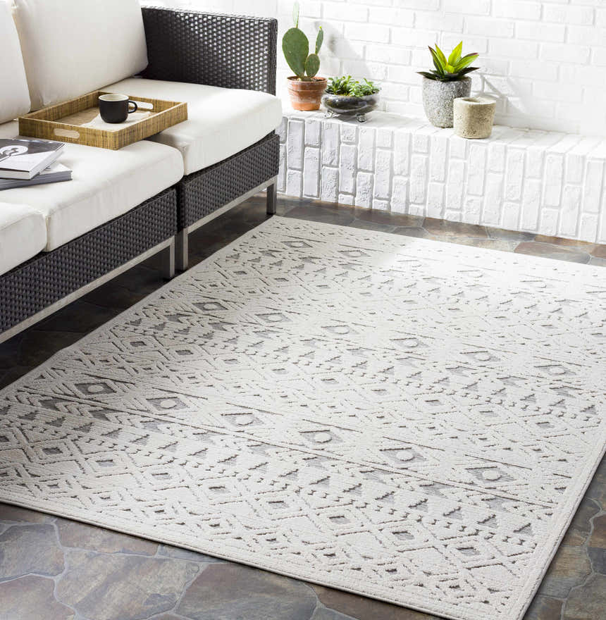 Outdoor patio scene with a light beige Mirani 3D Outdoor Area Rug, wicker sofa, and white brick wall. Roomscene-Rectangle