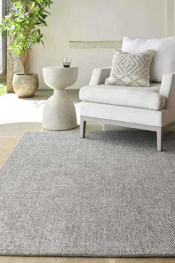 Neutral living room scene with a gray Medih Area Rug, white armchair, and modern side table. Roomscene-Rectangle