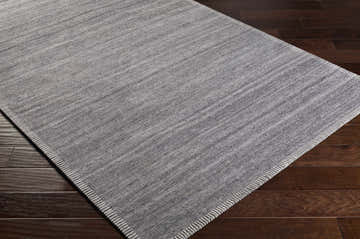 Close-up of the hand woven Millicent Carpet in charcoal and silver gray on dark wood flooring. Corner