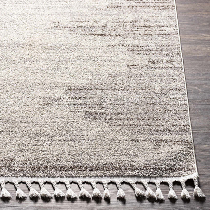 Close-up of the Malandag Area Rug, a machine-woven rug in dark brown, gray, and light gray with a textured design and tassel fringe. Front