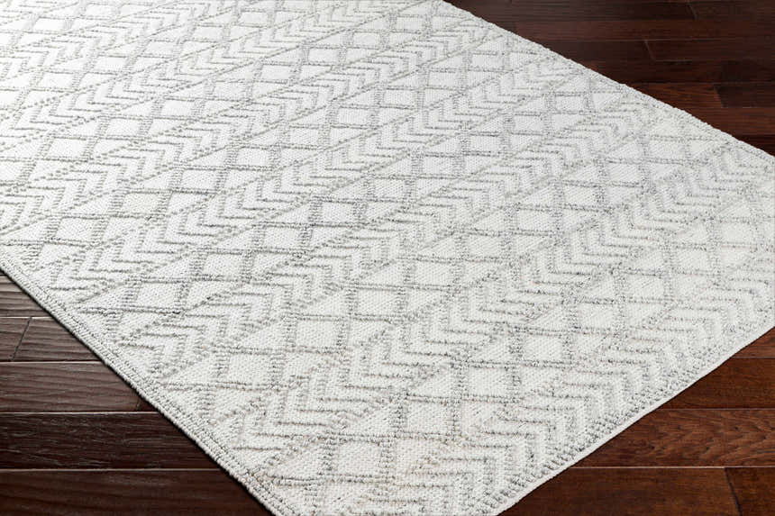 Close-up of the Meng Area Rug in charcoal and light gray with a geometric, hand-woven design on a dark wood floor. Corner