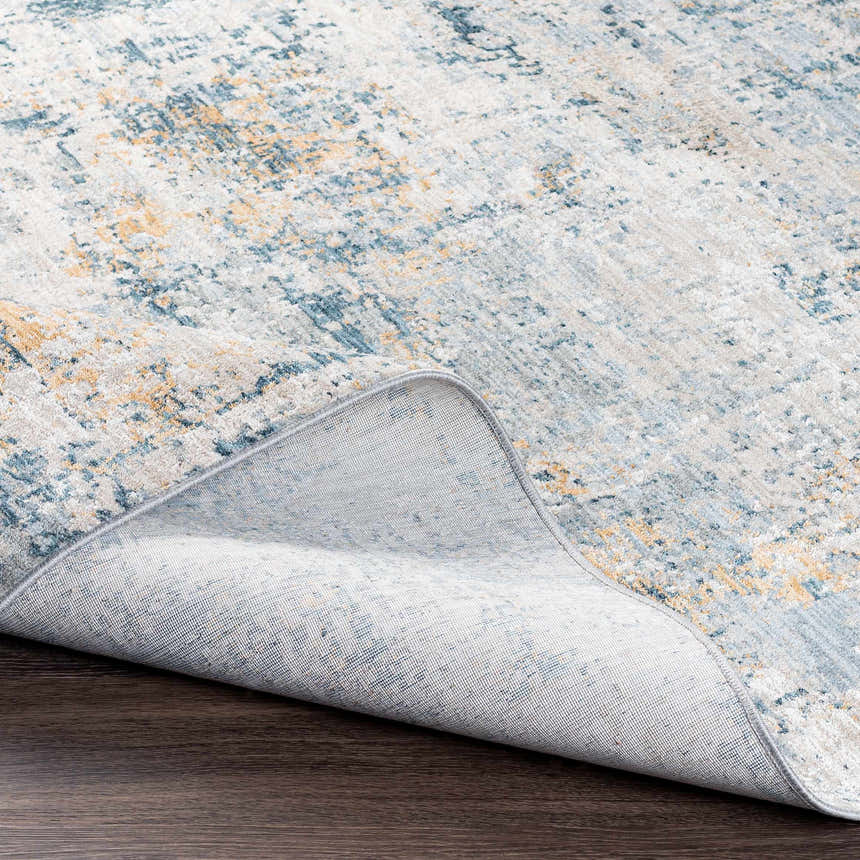 Close-up of the Montreat Luxe Rug showing its abstract pattern, cream, light gray, teal and mustard colors and machine woven construction. Fold