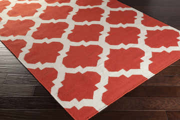 Close-up of the Moccasin Area Carpet showing a coral and cream geometric pattern on dark wood flooring. Corner