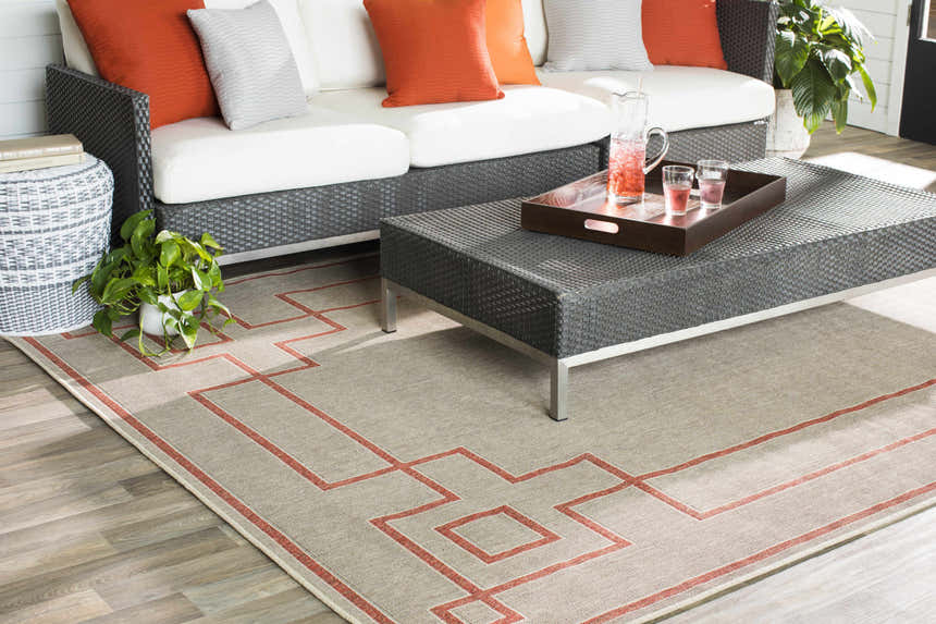Outdoor patio scene with a Moffett Area Rug in light beige and brick red, sofa, and coffee table. Styleshot