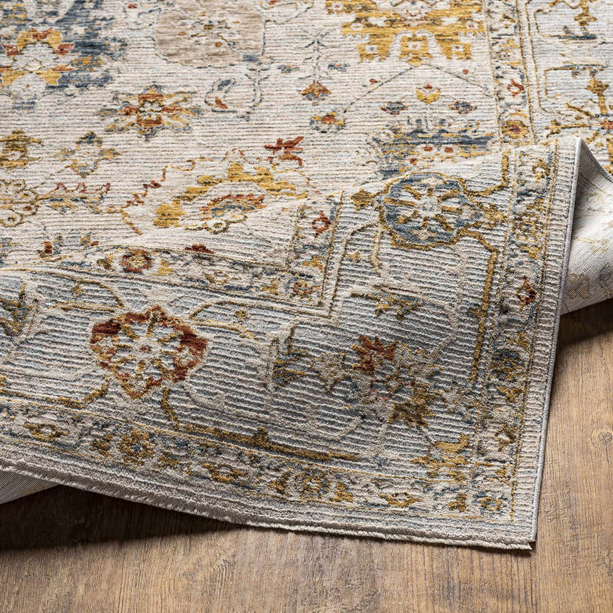 Close up of the Mogul Luxe Oushak Rug showing its brick red, cream, denim, and mustard floral pattern and textured weave. Fold