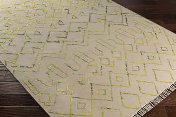 Close-up of the Monitor Area Carpet. Hand woven wool rug with geometric shapes in green, saffron, and light beige. Corner