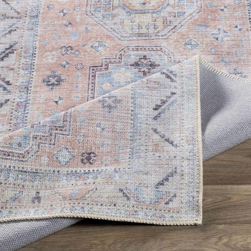 Close-up of the Morcott Peach Washable Area Rug. Features a traditional, bohemian pattern in peach, blue, and ivory. Fold