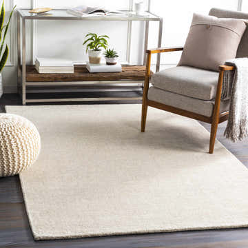 Living room scene with ivory Mariba Wool Area Rug, chair, pouf, console table, and plants. Roomscene-Rectangle